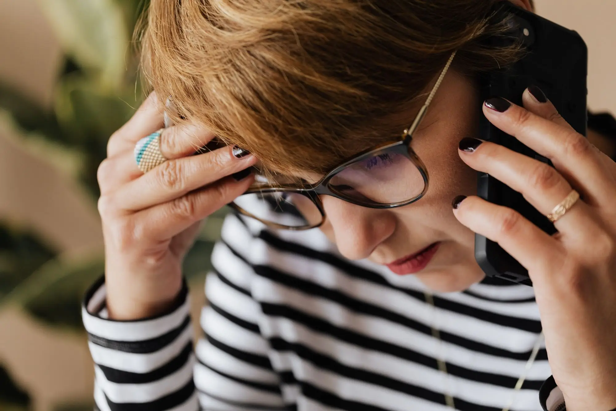 Worried business owner in glasses on the phone to her bank, hand to her forehead after spotting a scam payment