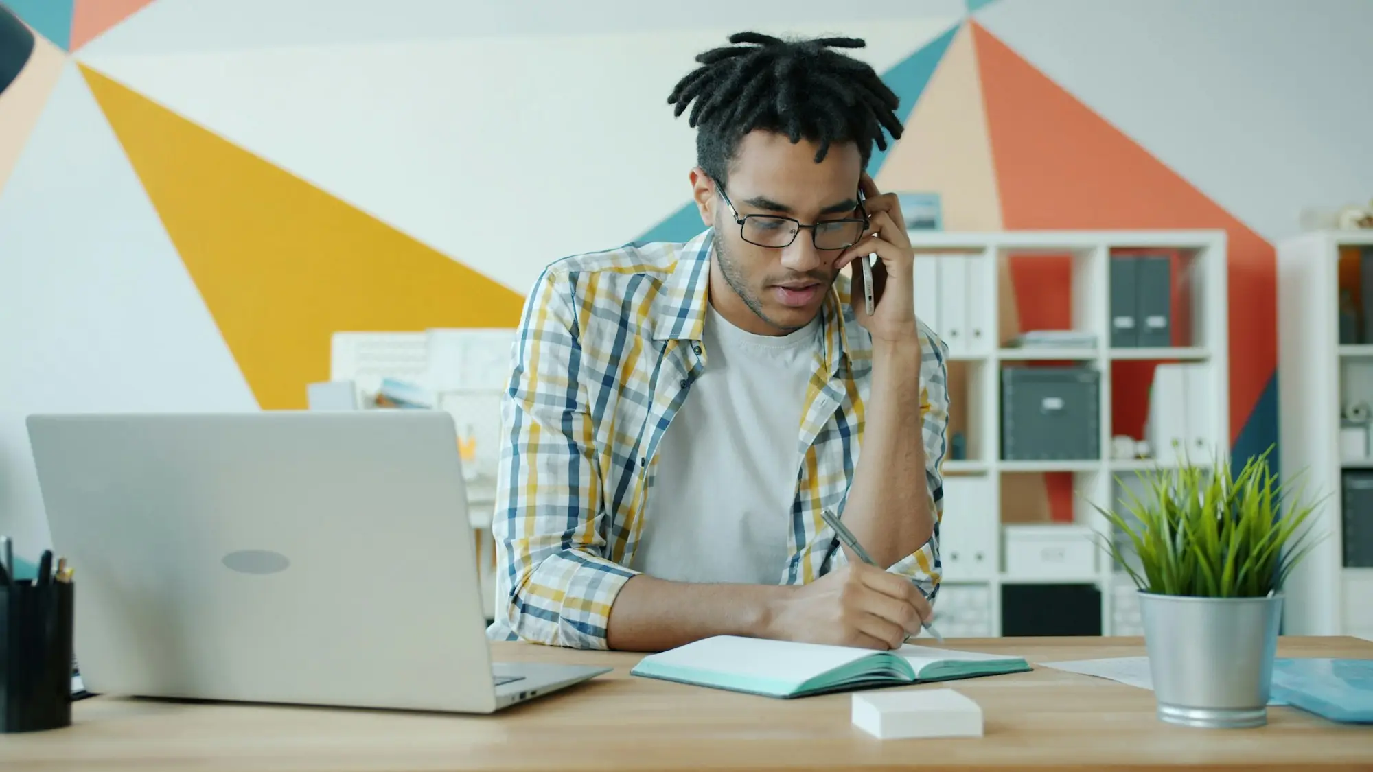 Business owner on the phone at his desk, noting invoice details beside a laptop