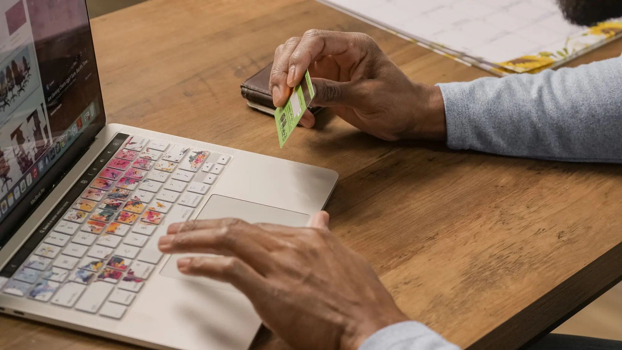 Business owner at a wooden desk holding a bank card in one hand while working through online banking on a laptop